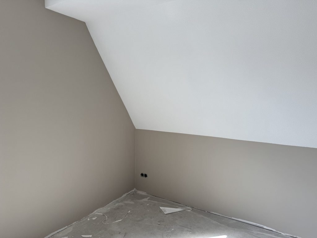 Zolderkamer met een schuine wand, strak afgewerkte muren in beige en een wit dakvlak