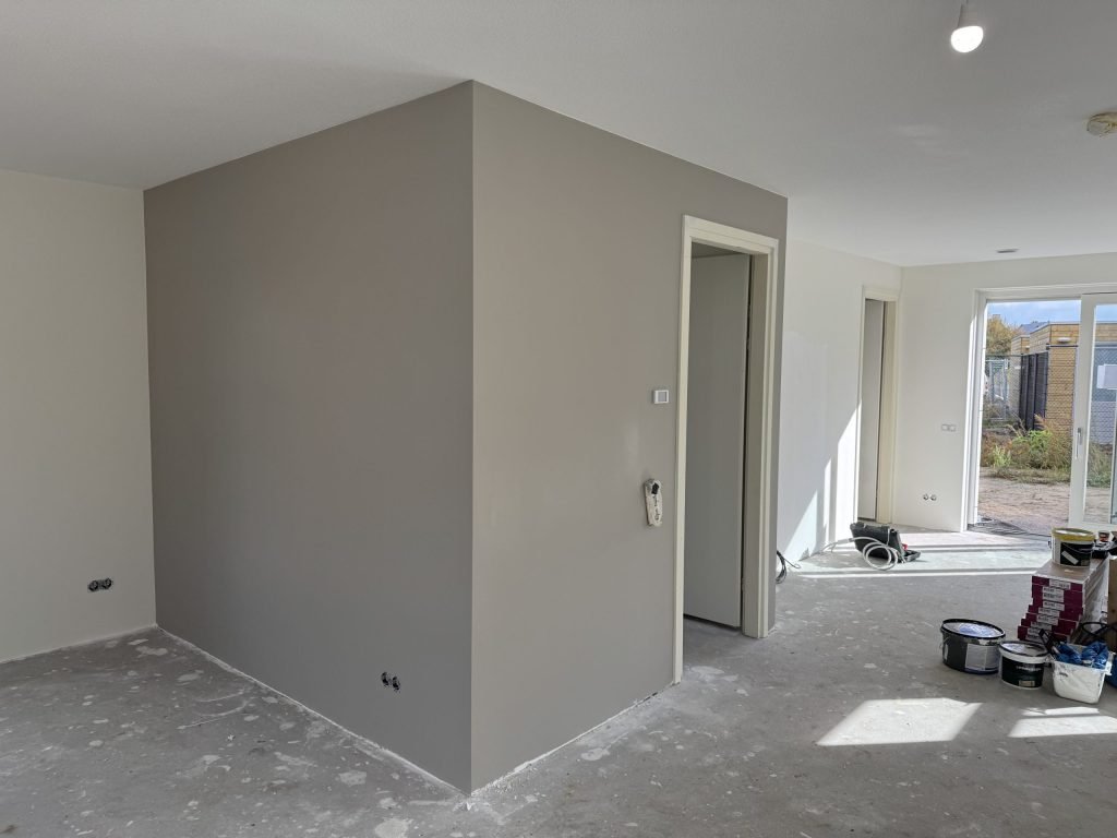Woonkamer met een strak gesausde grijze wand, open deur en verfemmers bij de tuindeuren