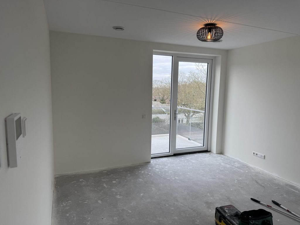 Lichte kamer met openslaande balkondeuren en gladde witte muren na het behangen